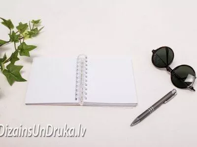 Atvērta piezīmju grāmata ar spirāles iesiešanu, pildspalvu un saulesbrillēm