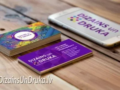 Uz koka galda izvietotas Dizains un Druka vizītkartes un viedtālrunis