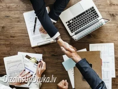 Biznesa partneru rokasspiediens virs galda ar klēpjdatoru un dokumentiem
