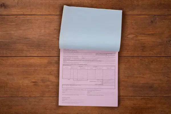 Custom carbonless forms pad with a lifted blue sheet and pink copy on a wooden surface