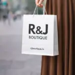White custom paper bag with R&J Boutique print in a woman's hand
