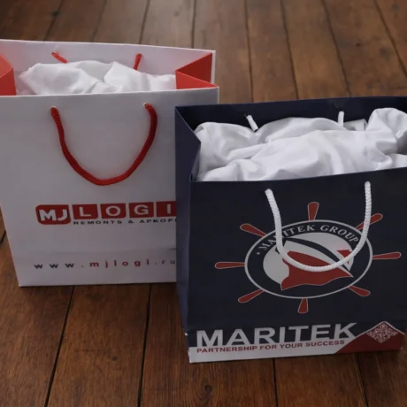 Two custom gift bags with print and cord handles on a wooden floor