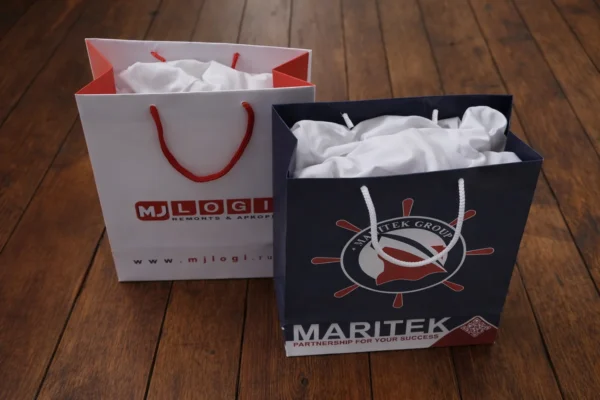 Two custom gift bags with print and cord handles on a wooden floor