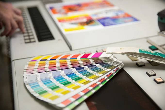 Color swatch fan on a desk beside a computer keyboard and printed sheets