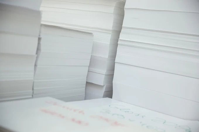 Close-up of stacks of white paper sheets, with a blurred page with a colorful pattern in the foreground