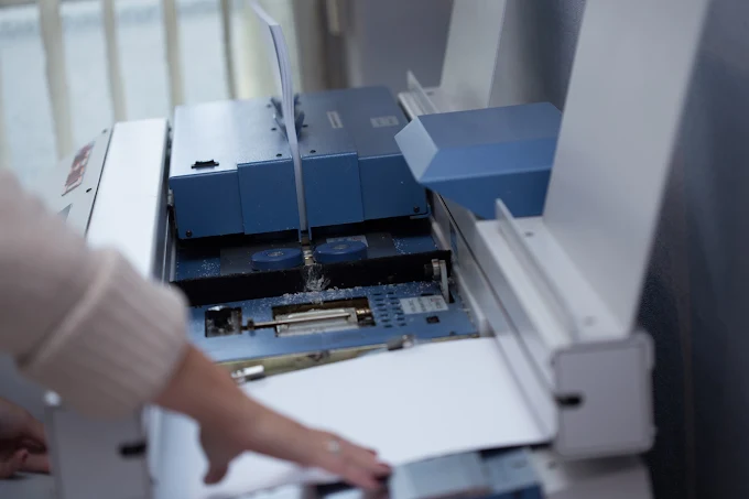 Hand inserting a sheet into a blue office machine or printer